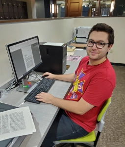 A person with light skin tone and short dark hair and wearing glasses is sitting in front of a computer. 