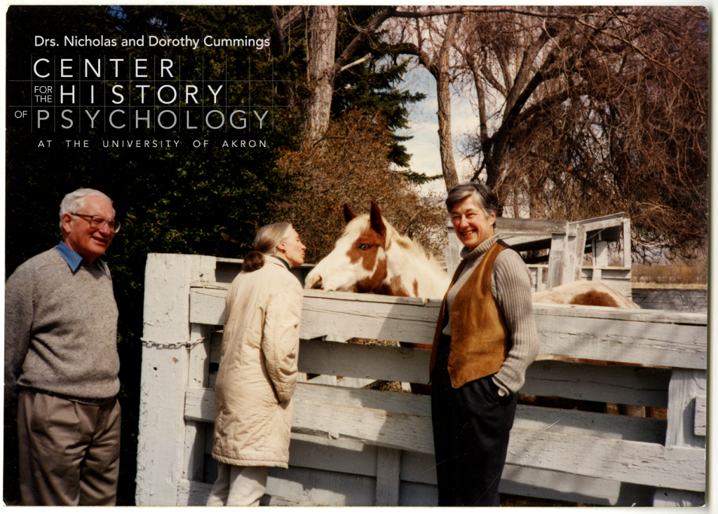 A photograph of three people standing outdoors. R. Allen Gardner is on the left. Jane Goodall stands in front of a white fence and leans toward a brown and white horse. Beatrix T. Gardner is on the right near the white fence and smiles at the camera.