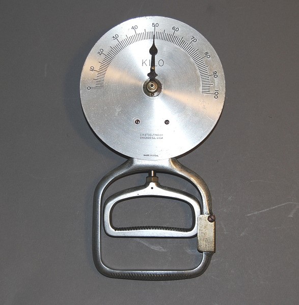 A metal disc with numerical markings and a moveable pointer. At its base is a handle, designed to be gripped by a single hand.